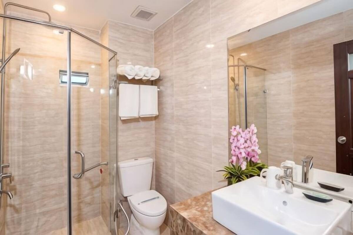 A modern bathroom with a glass-enclosed shower, a toilet, a sink with a mirror, and a potted orchid.
