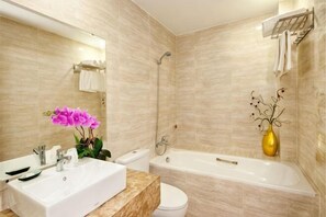 Une salle de bain équipée d’un lavabo, de toilettes, d’une baignoire et d’une douche. Un vase rempli de fleurs est posé sur le comptoir.
