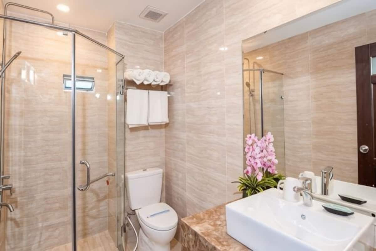 A modern bathroom with a glass shower enclosure, a white toilet, a marble countertop sink, and a large mirror.