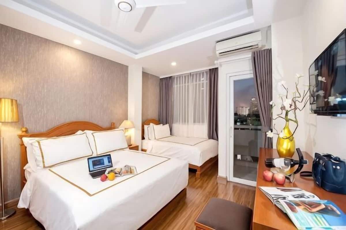 Hotelkamer met een groot bed, een kleiner bed, een bureau met een laptop, een vaas en uitzicht op de stad.
