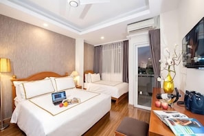 Habitación de hotel con una cama grande, una cama más pequeña, un escritorio con una computadora portátil, un florero y vistas a la ciudad.