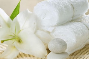 Una flor de lirio blanco, toallas enrolladas y una piedra sobre un tapete tejido.