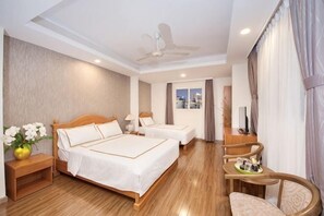 A hotel room with two beds, a desk, a chair, a ceiling fan, and a view of the city.