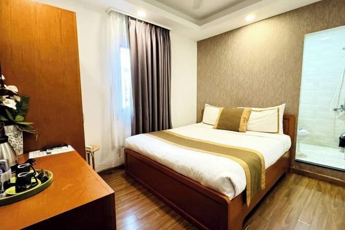 Een hotelkamer met een houten bed, een nachtkastje met een dienblad, een groot raam met gordijnen en een douche.
