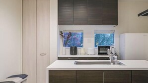 A modern kitchen with a white countertop, dark cabinets, a built-in microwave, and a window with a view. - UN-Villa (Tokyo)