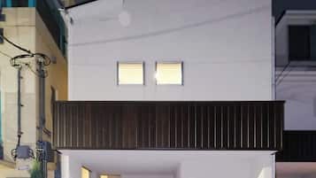 Een modern gebouw met een plat dak, twee kleine ramen en een donker houten balkon.