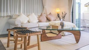 A modern living room with a glass coffee table, two wooden stools, a white sofa with cushions, and a vase with branches. - UN-Villa (Tokyo)