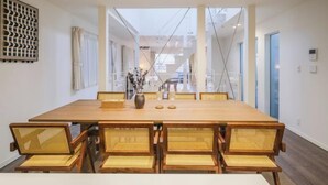 A long wooden dining table with six wicker chairs, a vase with flowers, and a geometric wall art piece. - UN-Villa (Tokyo)