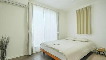 Un dormitorio con cama, mesita de noche, lámpara y ventana con cortinas.