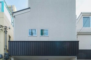 A modern building with a flat facade, two small windows, and a dark horizontal structure at the bottom. - UN-Villa (Tokyo)