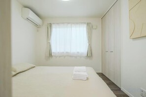 A bedroom with a bed, a window with curtains, a wardrobe, and an air conditioning unit. - UN-Villa (Tokyo)