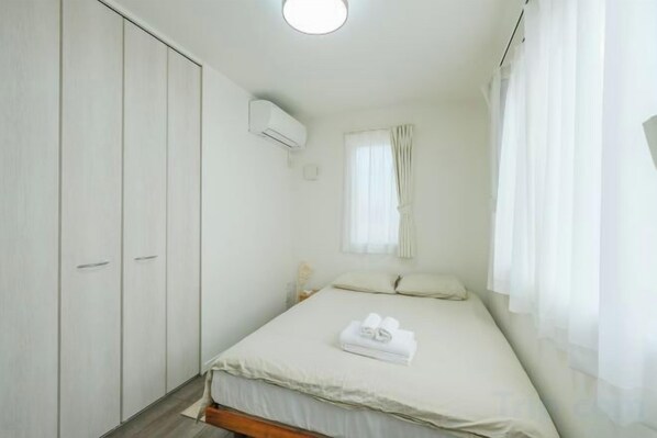A bedroom with a bed, a wardrobe, a window with curtains, and an air conditioning unit.