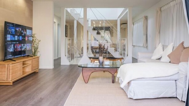A modern hotel room with a large bed, a glass table, and a TV displaying multiple screens. - UN-Villa (Tokyo)