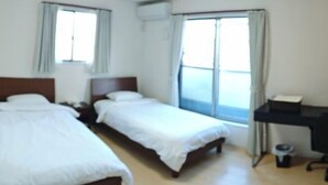Habitación de hotel con dos camas individuales, un escritorio y una ventana.