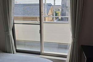 A room with a bed, a window with curtains, and a view of buildings outside.