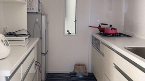 Una cocina compacta con armarios blancos, un microondas, un refrigerador pequeño, una ventana y un lavabo.