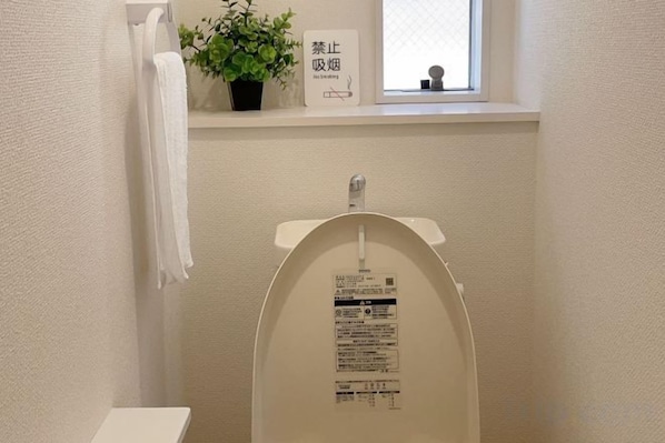 A toilet with a label, a towel hanging on the wall, and a window with a plant. - YOUJIAN B&B (Tokoname)