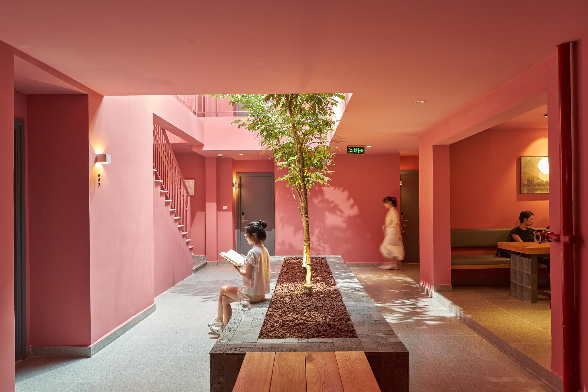 A corridor with a central tree planter, a staircase, and a seating area with a table.