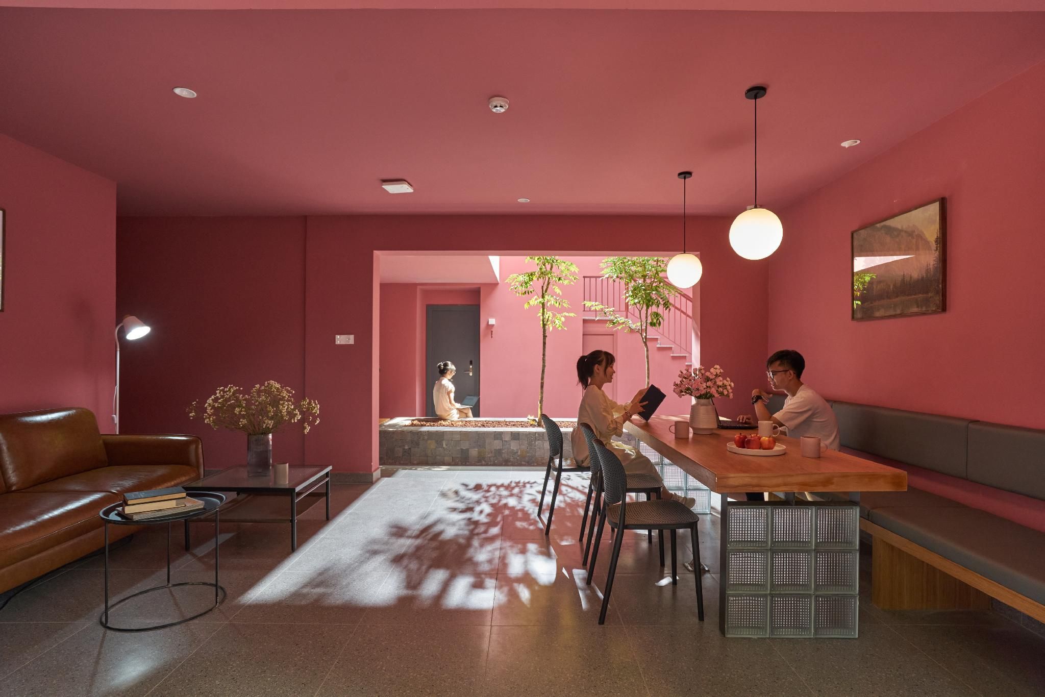 A modern living room with a pink color scheme, a dining area with a wooden table and chairs, and a sofa.