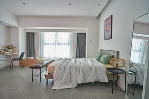 A modern bedroom with a bed, bedside table, chair, desk, and large windows.