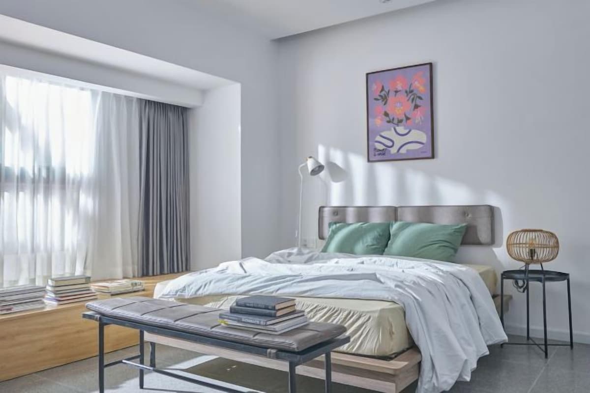 A modern bedroom with a bed, bedside table, lamp, and a framed artwork on the wall.