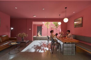 A modern living room with a pink color scheme, a dining area with a wooden table and chairs, and a sofa.