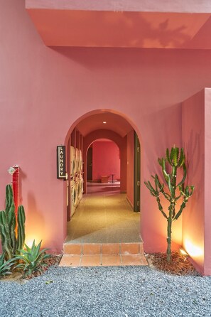 Un couloir avec un mur rose, une enseigne indiquant « LAUNDRY » et des cactus de chaque côté.