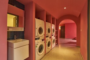 Une salle de bain d’hôtel avec une rangée de machines à laver superposées, un lavabo et un miroir.