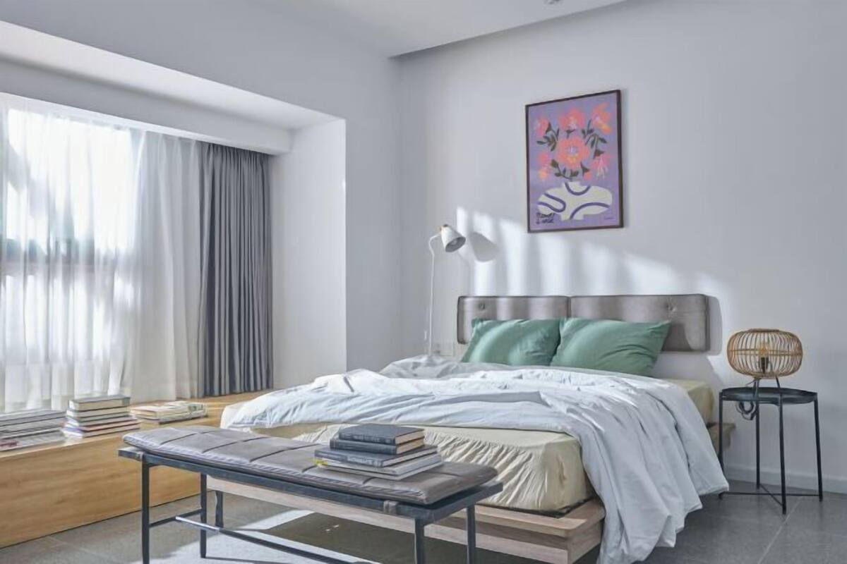 Ein modernes Schlafzimmer mit Bett, Nachttisch, Lampe und einem gerahmten Kunstwerk an der Wand.
