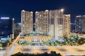 A high-rise building complex with multiple floors, surrounded by a well-lit area with trees and a road. - Luxury Serviced Apartment Vinhomes D’Capitale Hanoi – Zen Homes (Hanoi)