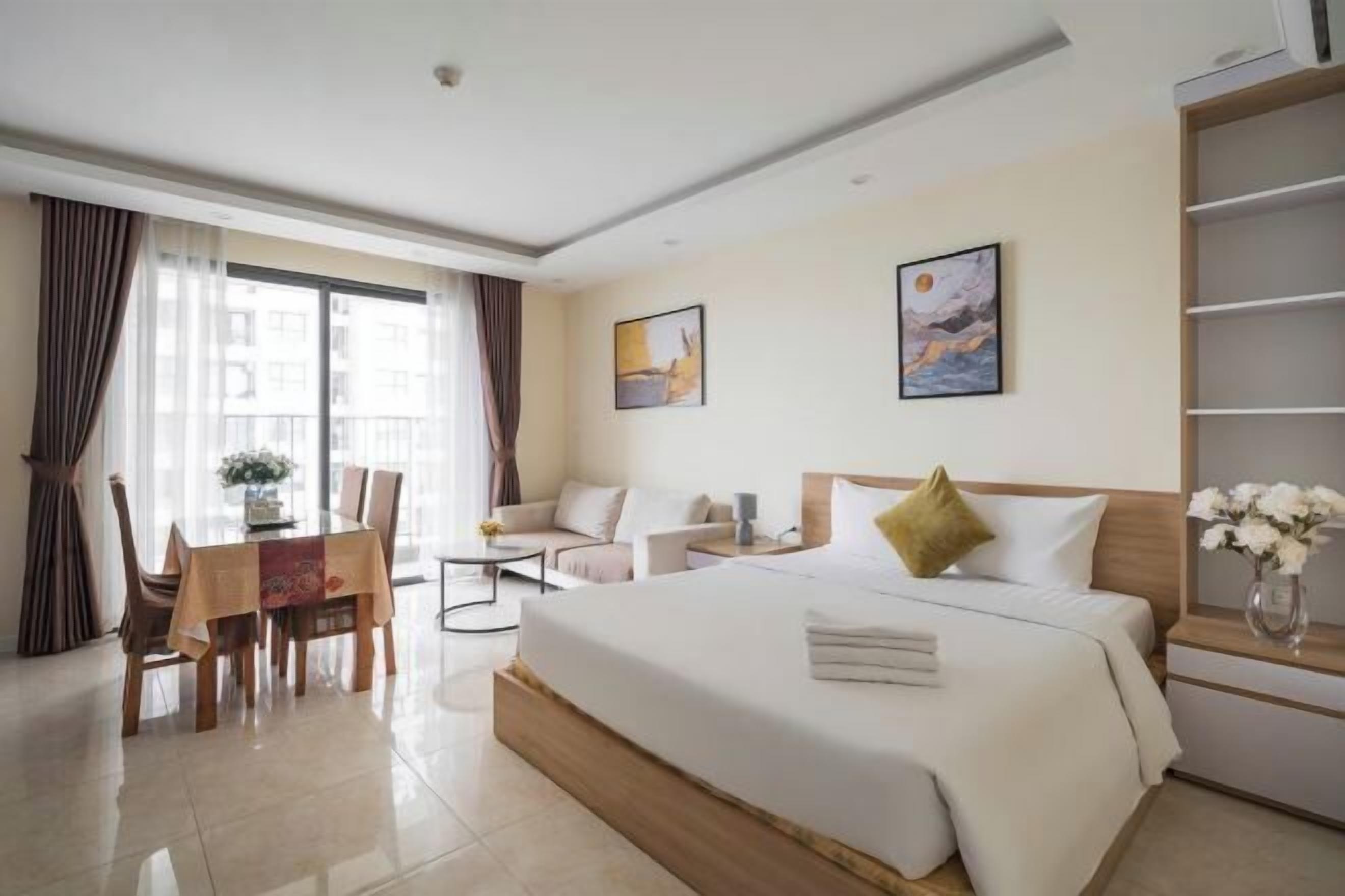 A hotel room with a bed, a seating area with a table and chairs, a bookshelf, and artwork on the walls.
