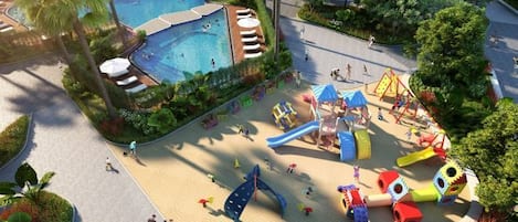 A children's play area with slides and climbing structures, surrounded by a pool and greenery.