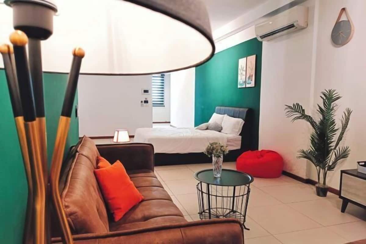 A modern living room with a brown sofa, a round coffee table, a red bean bag, and a bed with a white duvet.