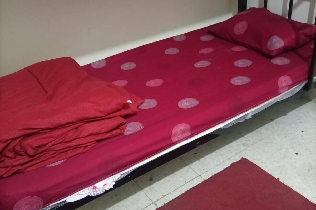 Una cama individual con una manta roja y una almohada a juego, una pared blanca y una alfombra roja en el suelo.