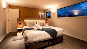 A hotel room with a large bed, a wooden headboard, bedside lamps, a night sky view, and a carpeted floor. - Modern 3 Bedroom Home in Wanaka with Mountain View (Wanaka)