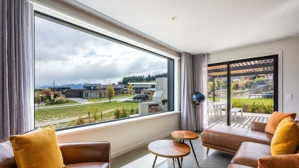 A modern living room with a large window, leather sofas, and a small round table. - Modern 3 Bedroom Home in Wanaka with Mountain View (Wanaka)