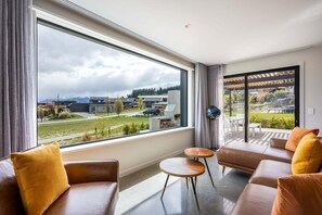 A modern living room with a large window, leather sofas, and a small round table. - Modern 3 Bedroom Home in Wanaka with Mountain View (Wanaka)