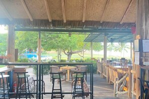 An outdoor seating area with tables and chairs, a thatched roof, and a view of a pool and trees. - Better view koh yao yai (Koh Yao Yai)
