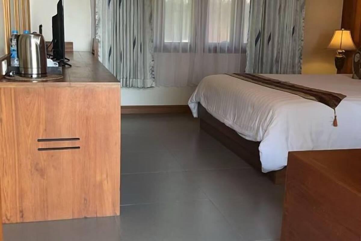 Une chambre d’hôtel avec un lit, un bureau en bois, une bouilloire et une lampe.
