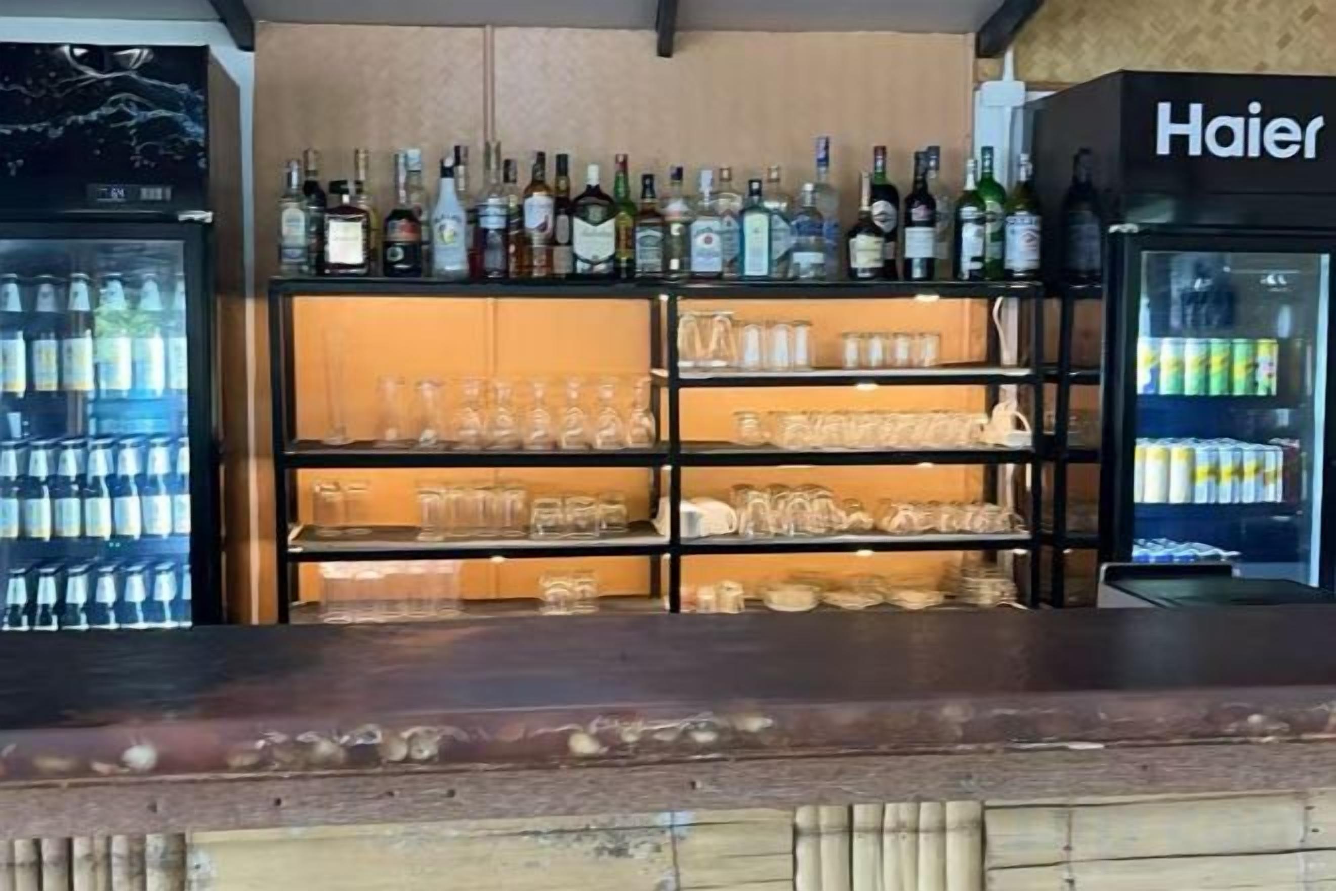 A bar area with shelves of bottles and glasses, a refrigerator, and a Haier branded appliance.