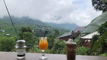 A table with three drinks and a bottle, overlooking a mountainous landscape.