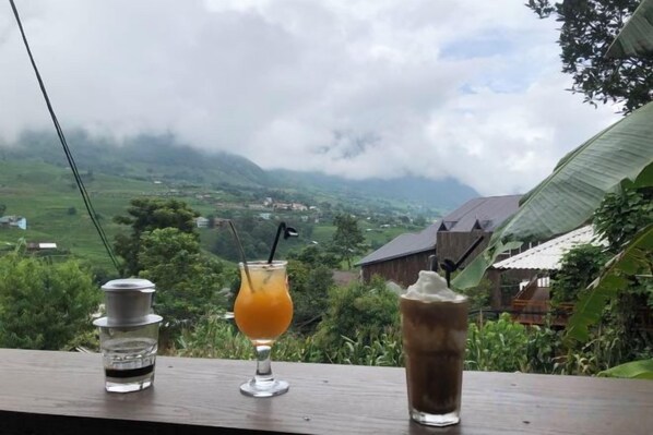A table with three drinks and a bottle, overlooking a mountainous landscape.
