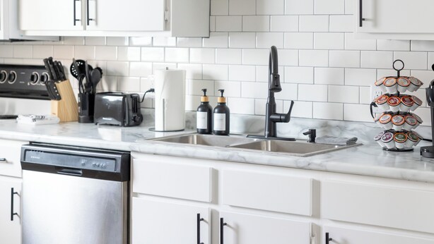 Una cocina moderna con armarios blancos, un lavavajillas de acero inoxidable, un fregadero y una máquina de café.