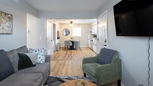 Una sala de estar con un sofá gris, un sillón verde, una mesa de centro de madera y un televisor montado en la pared.