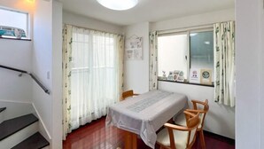 Un área de comedor con una mesa y sillas, una ventana con cortinas, un cuadro en la pared y una escalera con barandilla.