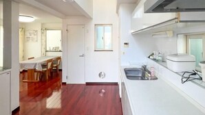 Una cocina con mostrador blanco, un fregadero y una ventana sobre el fregadero. Hay una puerta que conduce a otra habitación.