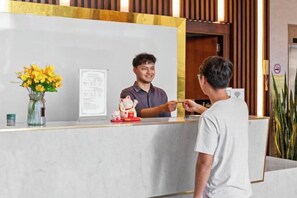 A reception desk with a whiteboard, a vase of yellow flowers, and a small red figurine. - Diamond Beach Hotel (Da Nang Municipality)