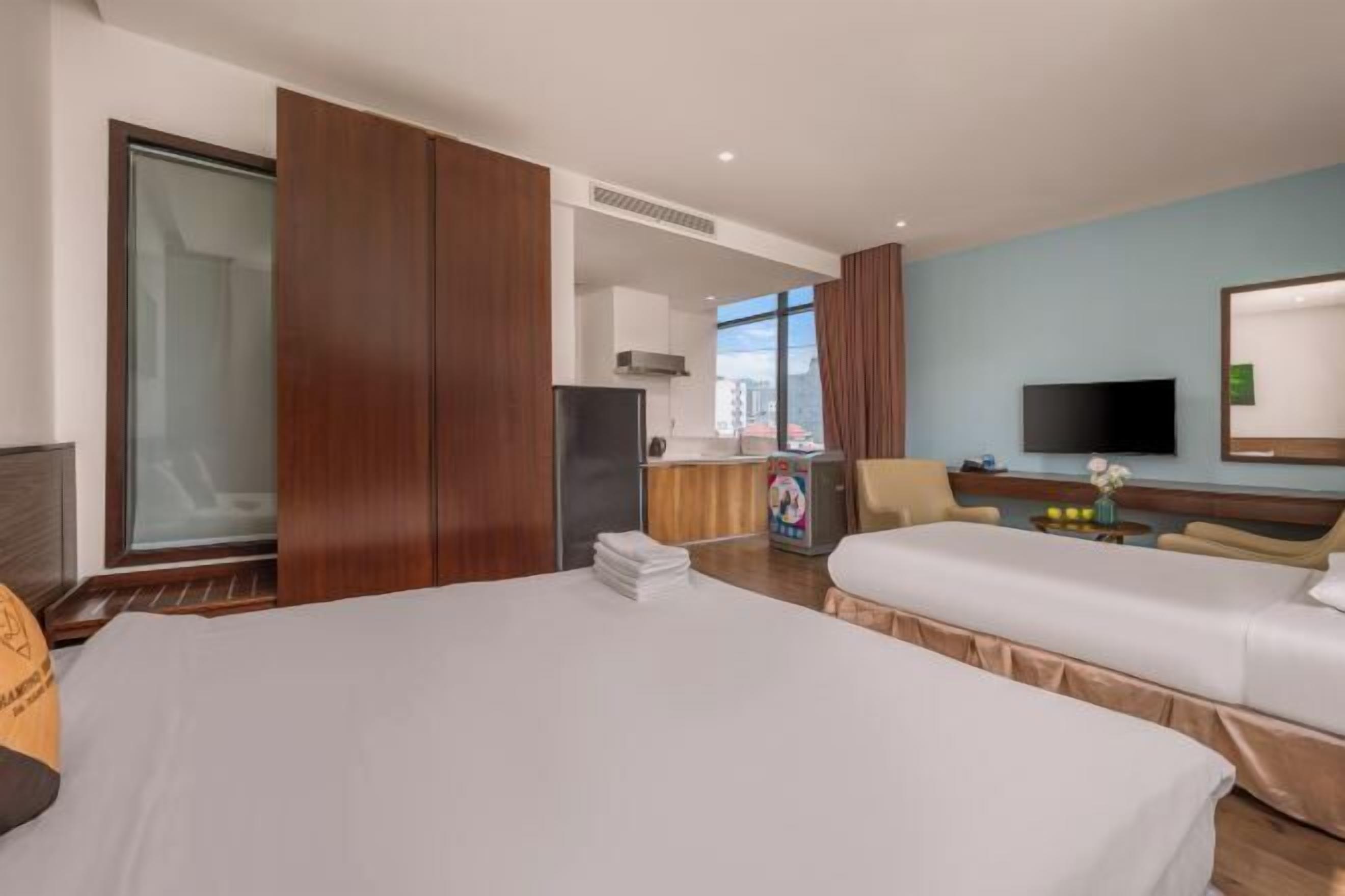 Habitación de hotel con dos camas, televisión, kitchenette pequeña y vista a la ciudad.