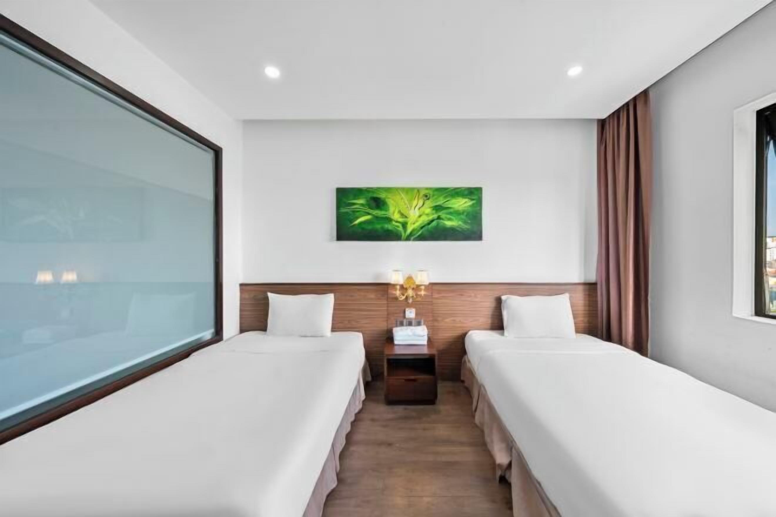 A hotel room with two beds, a nightstand with a lamp, a green abstract painting, and a large window.