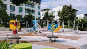 A playground with swings, slides, and a yellow bus model. - Utopian Residence IMAGO Mall KK (Kota Kinabalu)